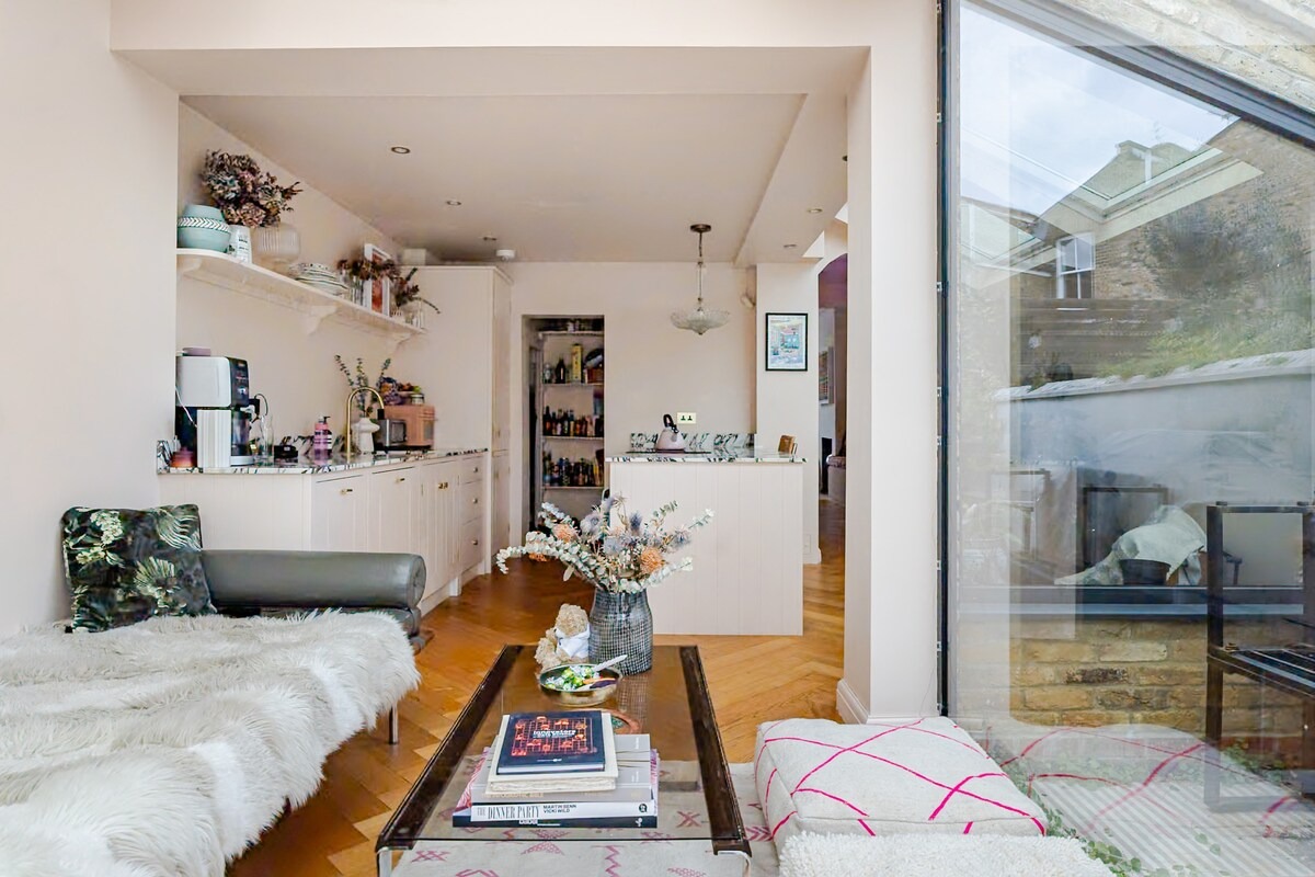 Open plan pink living space with sheepskin-draped daybed and glass wall