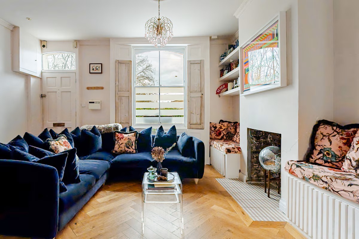 A living room with a deep navy velvet sofa, herringbone parquet and a vintage teardrop chandelier