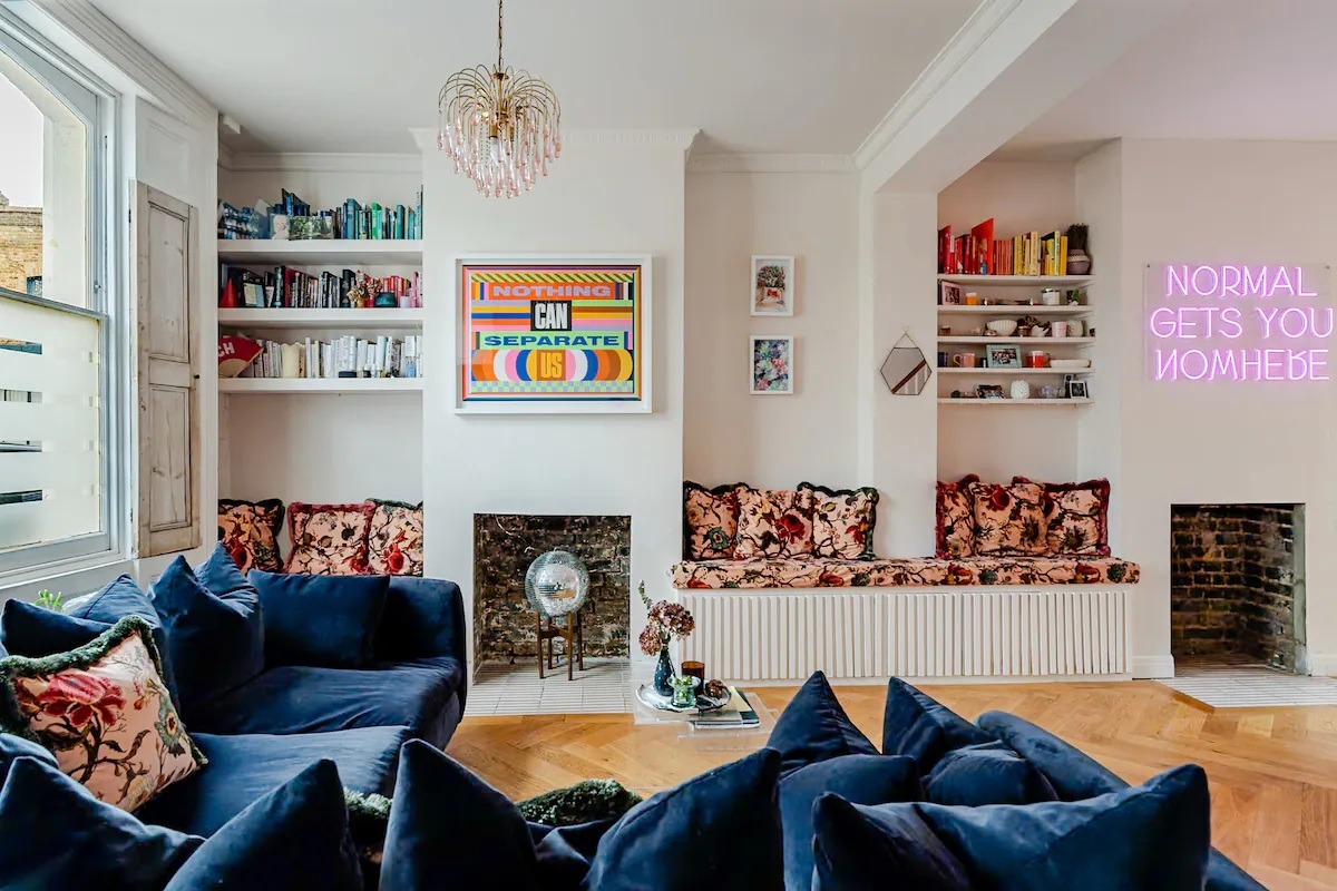 Living room with navy velvet sofas, floral window seats and a pink neon sign