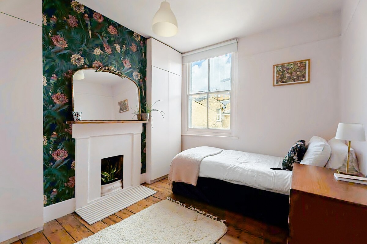 Bedroom with dark botanical wallpaper and antique gilt mirror