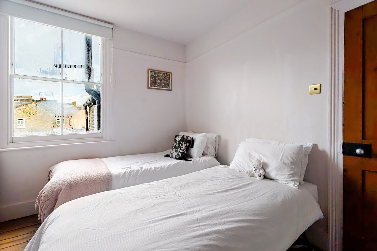 A calm twin bedroom with pale pink throws and warm timber door